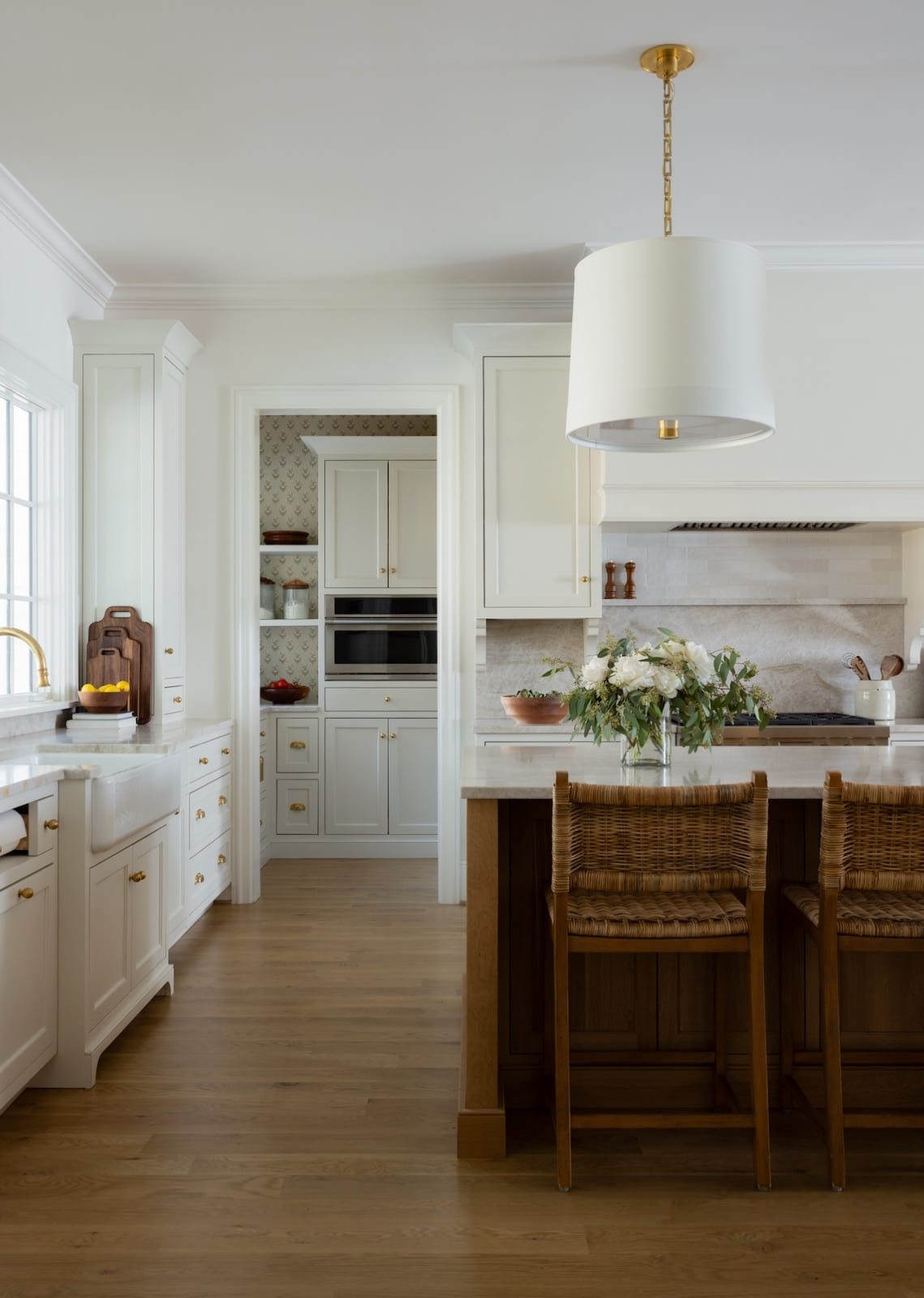 Kitchen at Meadowbrook Cottage with pale cabinetry, a marble island, rattan counter stools and a walk-in pantry beyond