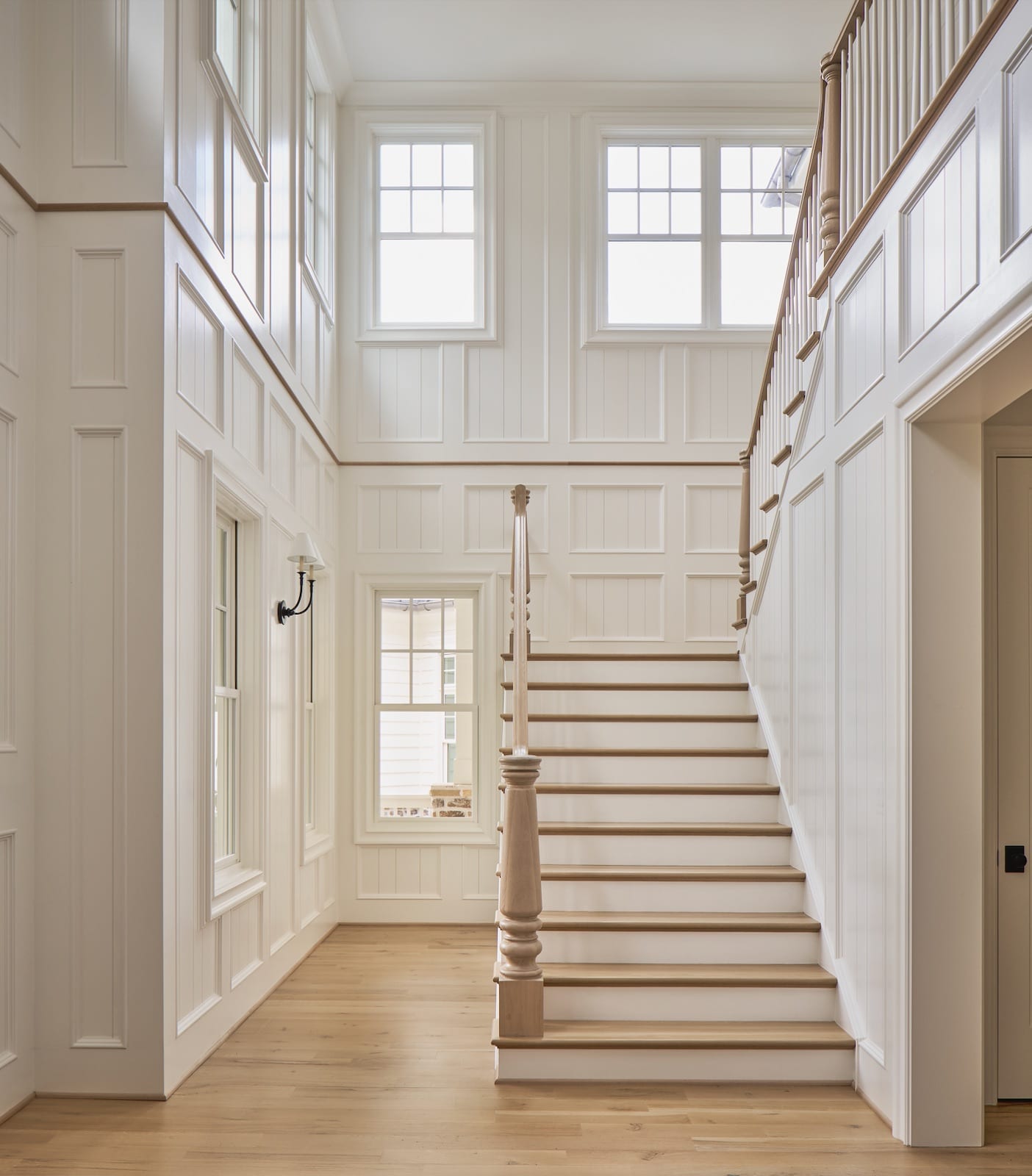 Two-story stair hall at Meadowbrook Cottage with paneled walls, a turned newel post and abundant natural light