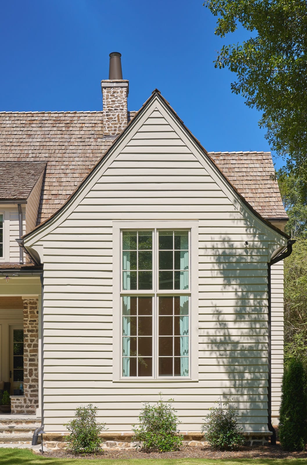 Gable end of The Potter House in cream clapboard with a stone chimney and cedar-shake roof