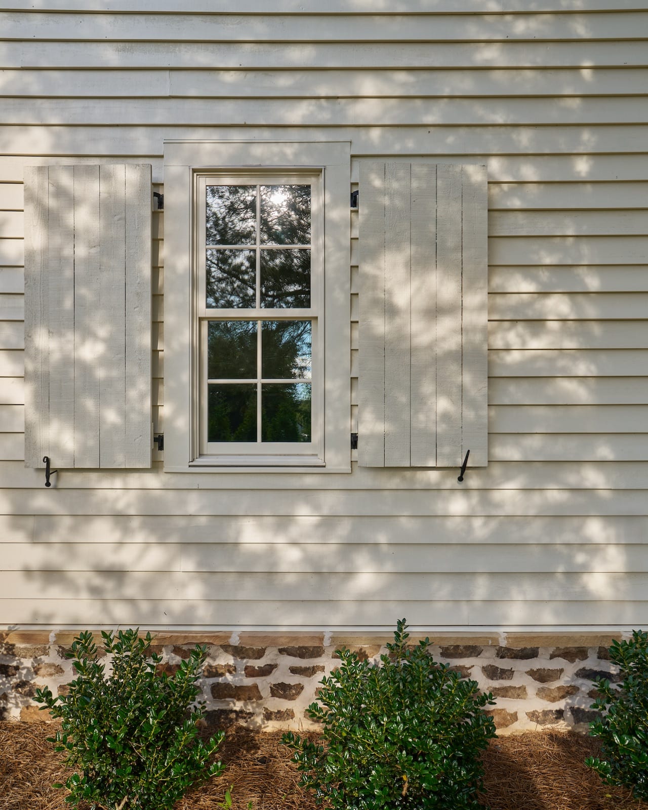 Exterior detail of The Potter House, a shuttered window on cream clapboard above a stone foundation