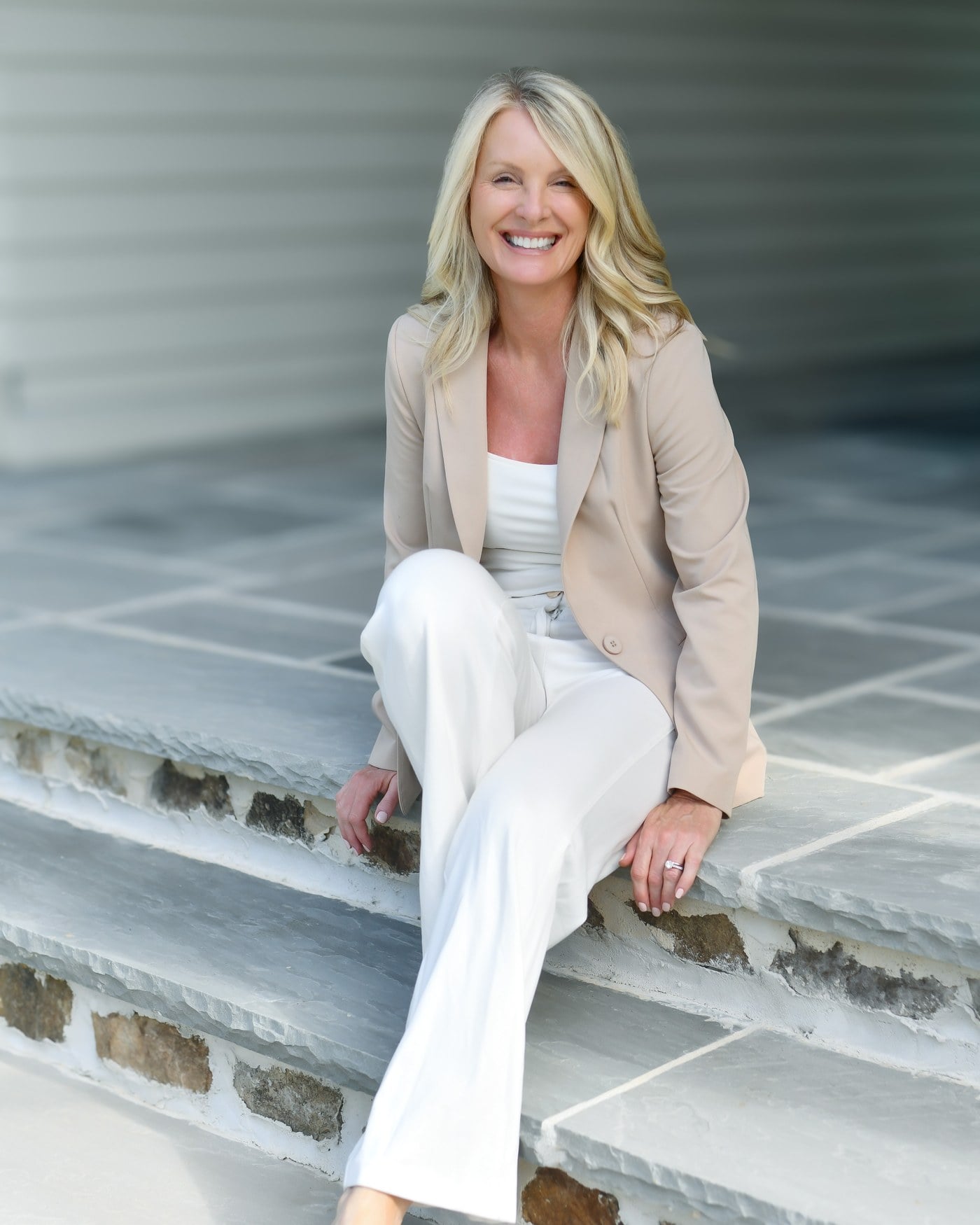 Kim Hedrick, Broker and REALTOR® with the Andy Bovender Team at Compass, seated on stone steps in a tan blazer